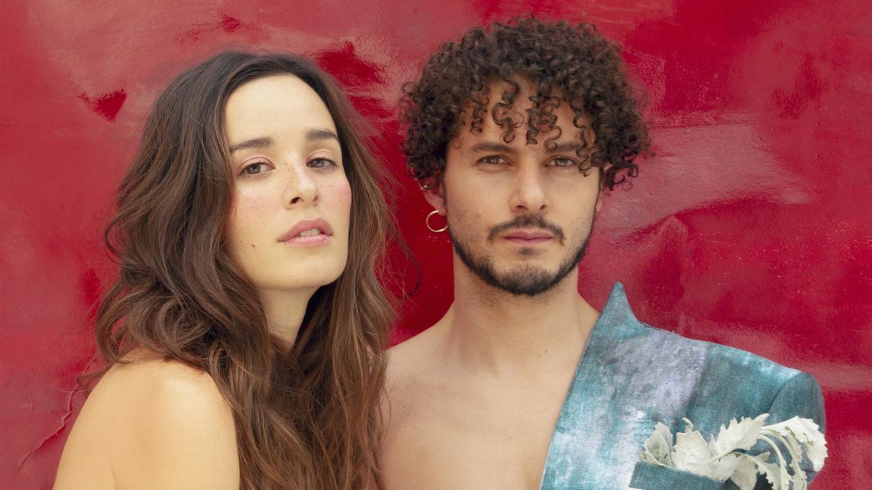 A woman and a man with curly dark hair against a painterly red backdrop