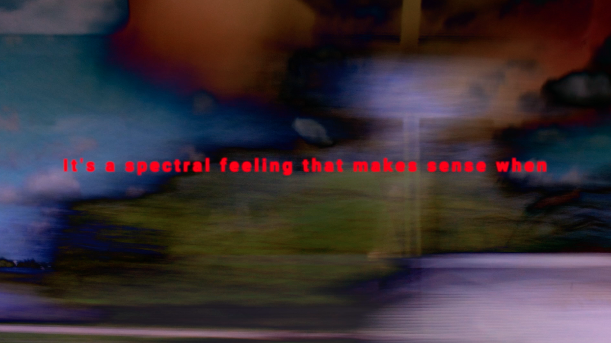 a still from a film that shows a blurred background of olive green, purple, blue and brown, with the words in red "it's a spectral feeling that makes sense when"