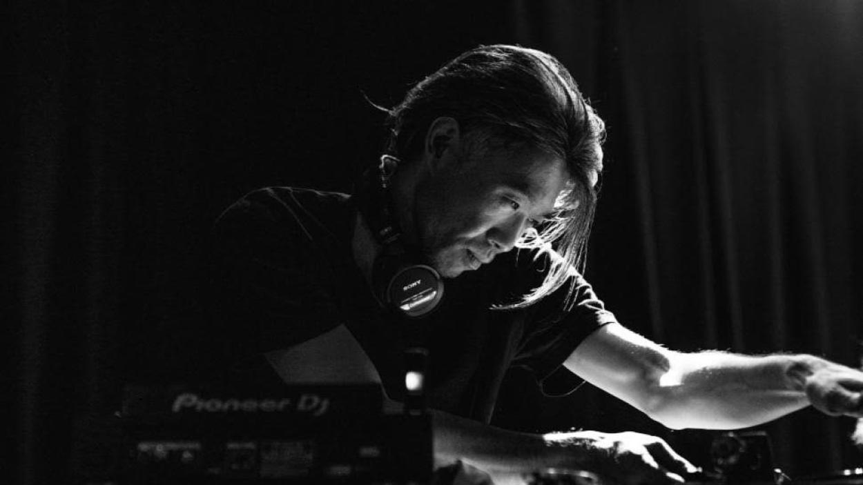 A black an white image of a man wearing a black tee shirt leaning over a turntable