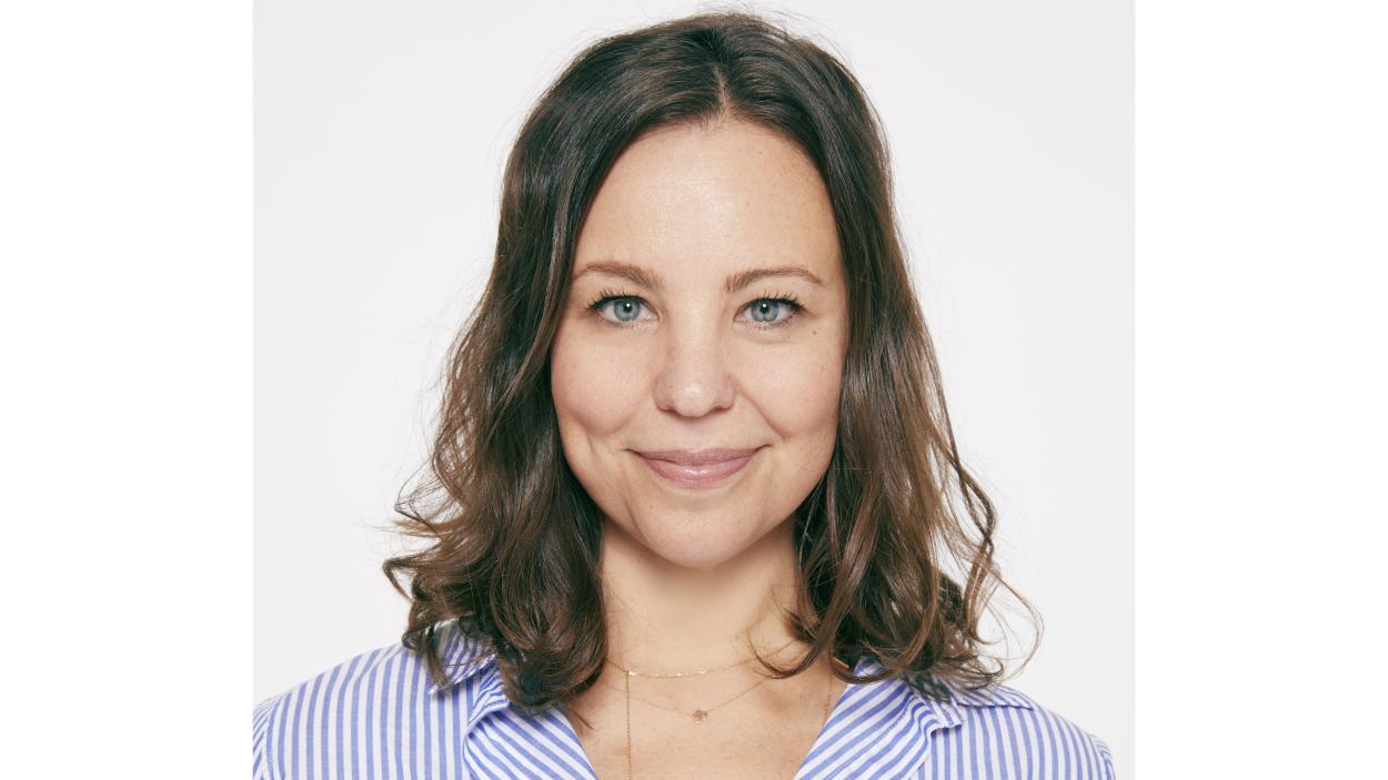 A headshot of a light skinned woman with wavy, brown, shoulder length hair and blue eyes
