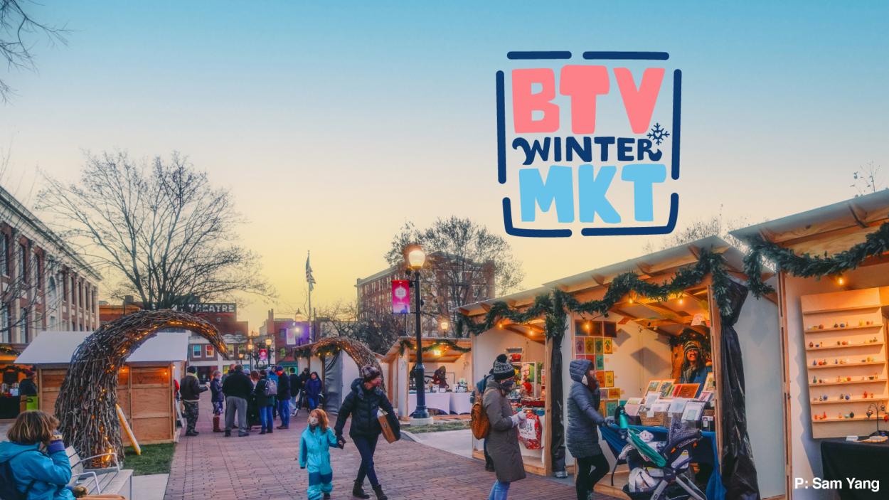 btv_winter_mkt_1600x900.jpg people walk amongst a cluster of vendor stalls decked with evergreen garlands and white twinkle lights under a sky that ombres from blue to yellow as the sun sets.