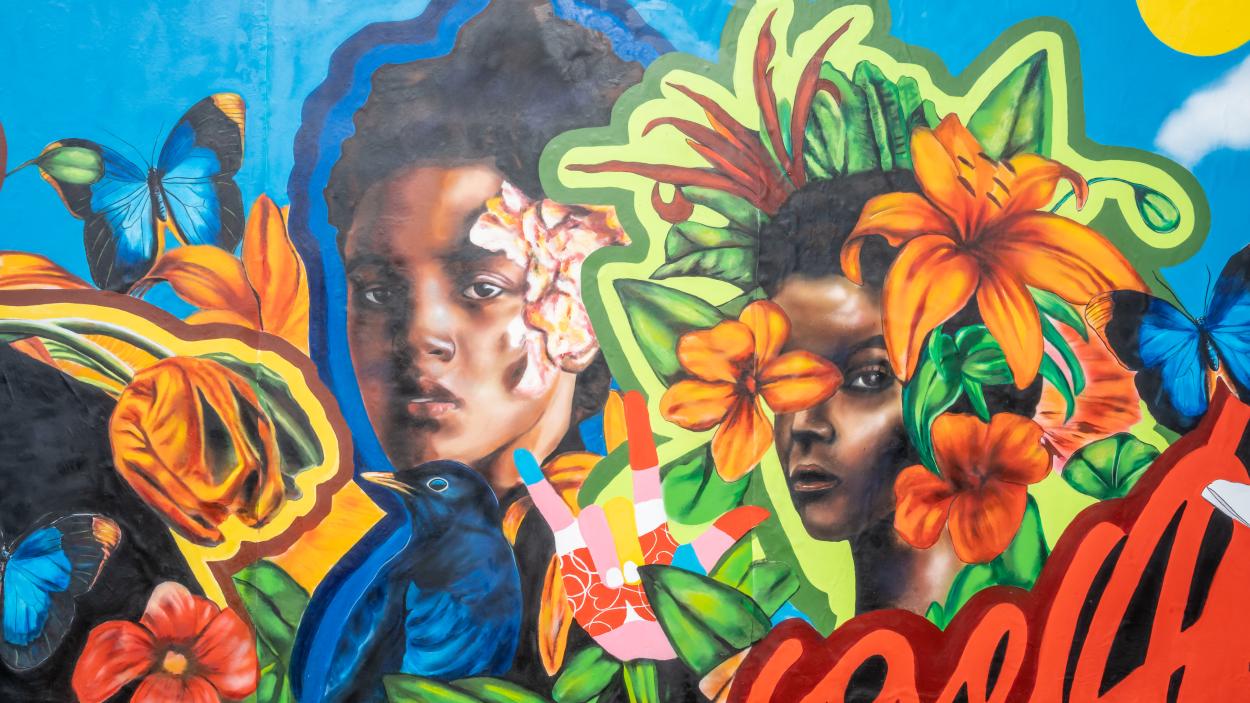 A closeup of a mural featuring a portrait of two girls and bright blooms of flowers against a sky-blue background with &quot;A Love Supreme&quot; written beneath them.