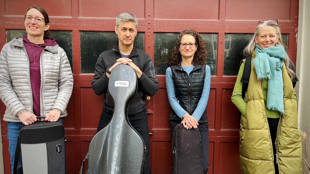 eclectica_sunday_classical_8_27.jpeg Four people stand against a red garage door. Three are light skinned women and one is a light skinned man holding a grey cello case