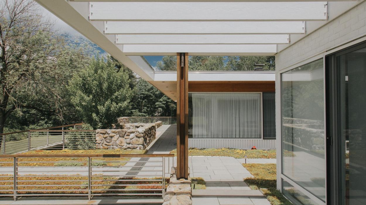 A photograph of the exterior of a modern home, with large glass windows and and an angular white overhang