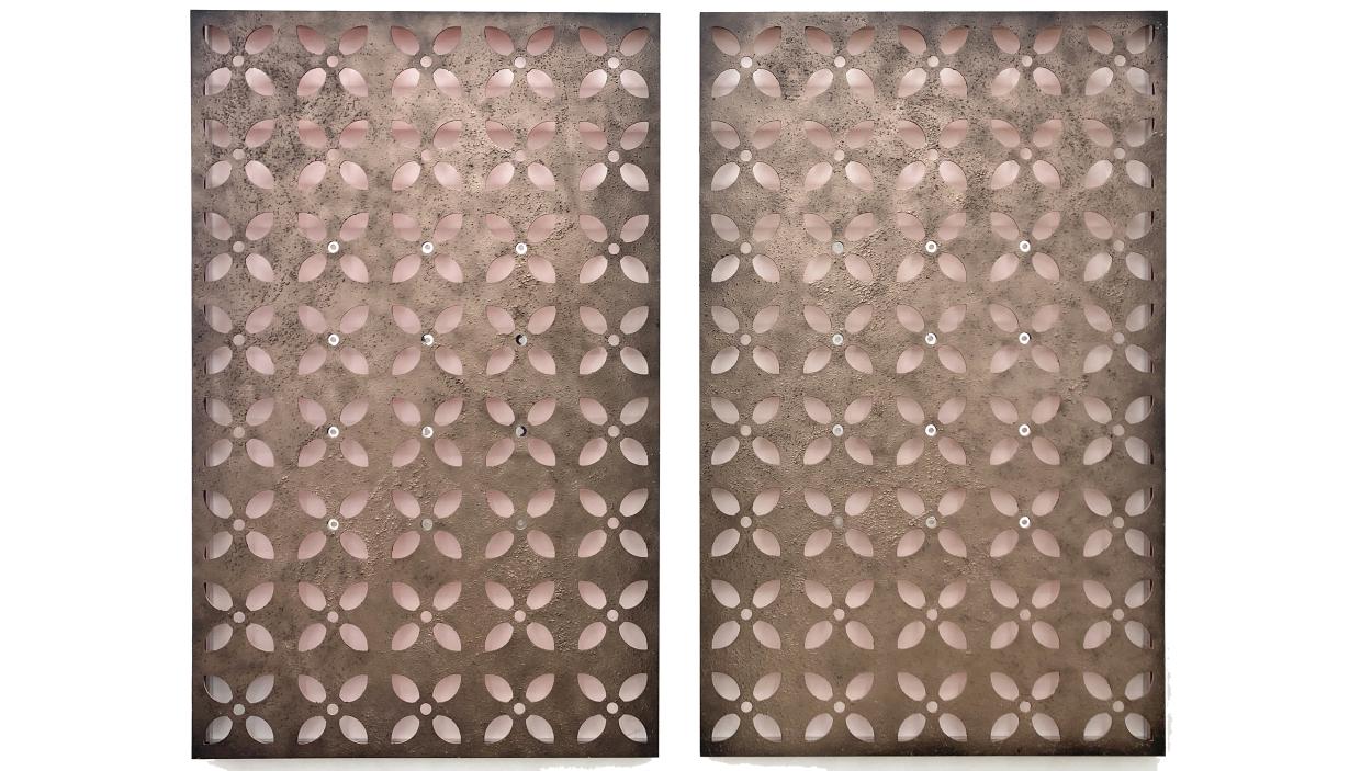 A photograph of a sculpture that consists of two rectangular flat metal panels with rows of geometric floral shapes stamped out.