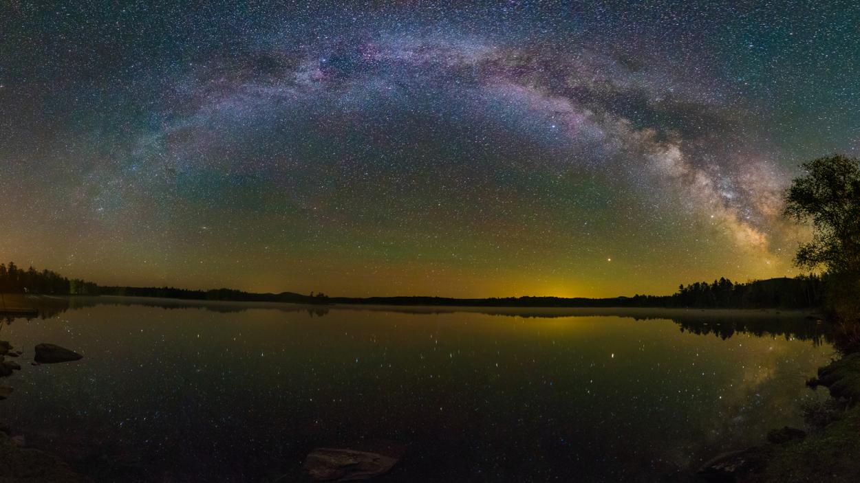 A long exposure color photograph of a nebula over a lake