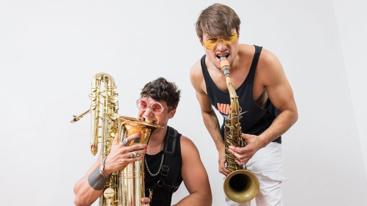 Two gentlemen in tank tops and sunglasses pose with saxophones.
