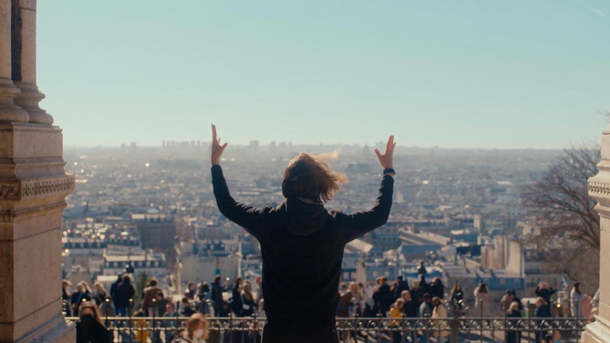 An image of a person with their back to their camera, addressing a crowd, with their arms raised.