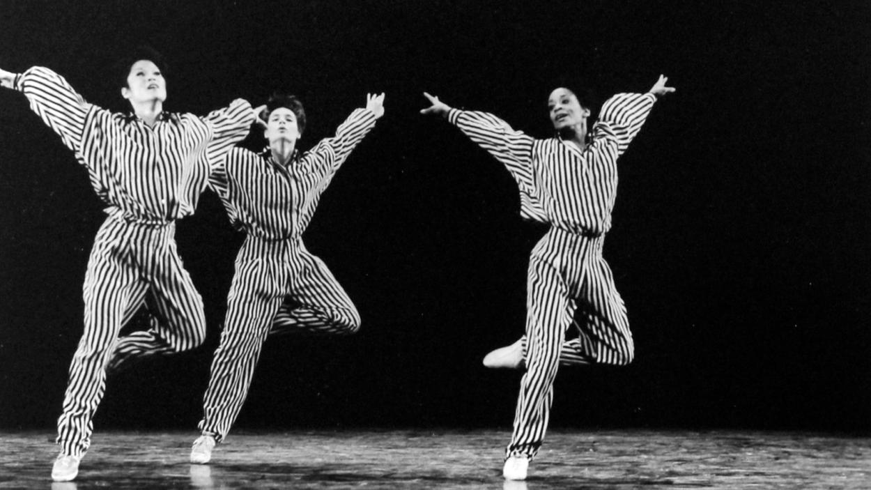 A black and white image of three dancers with one leg up and their arms extended