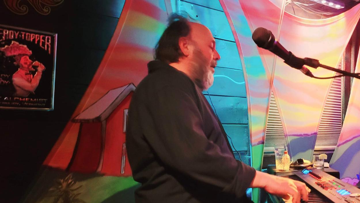man with bright fabric behind him singing into mic.