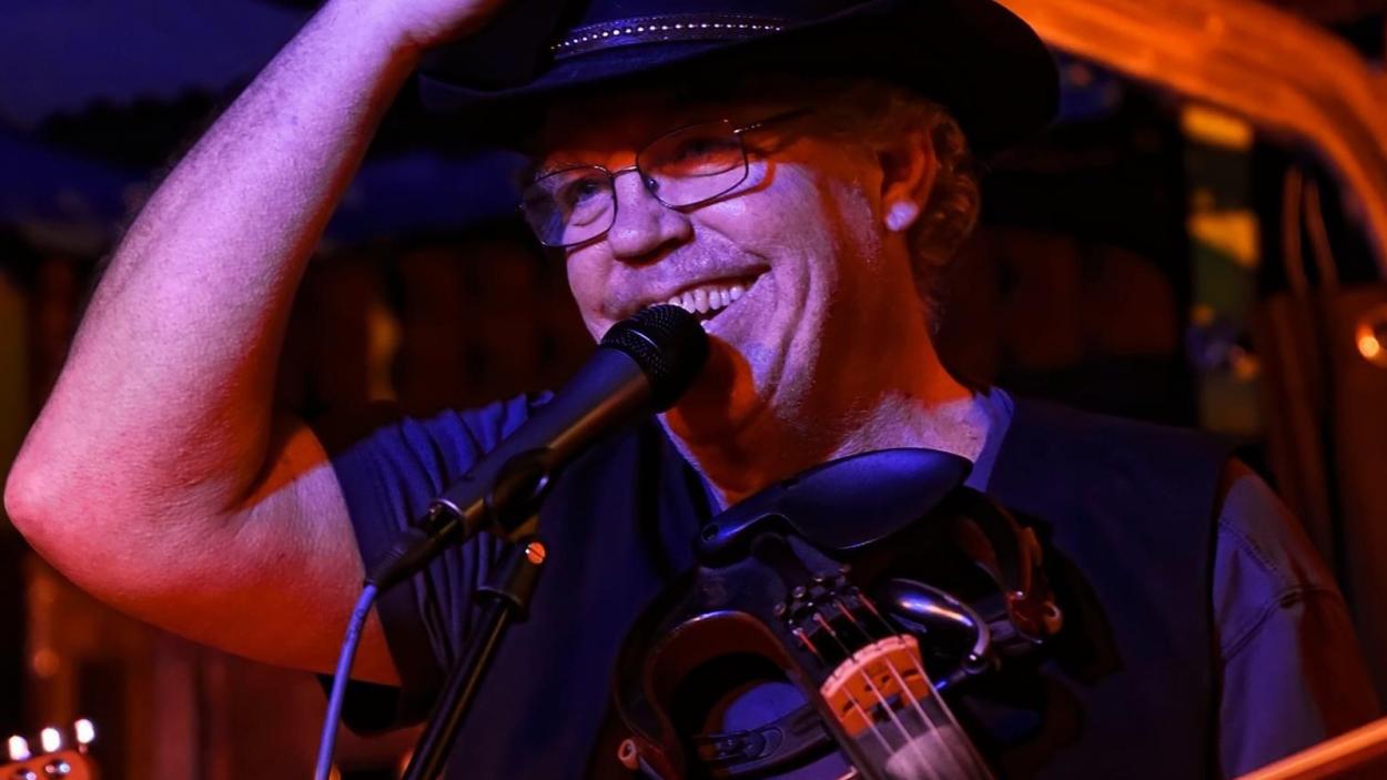 a man with glasses smiling into a mic with pink light
