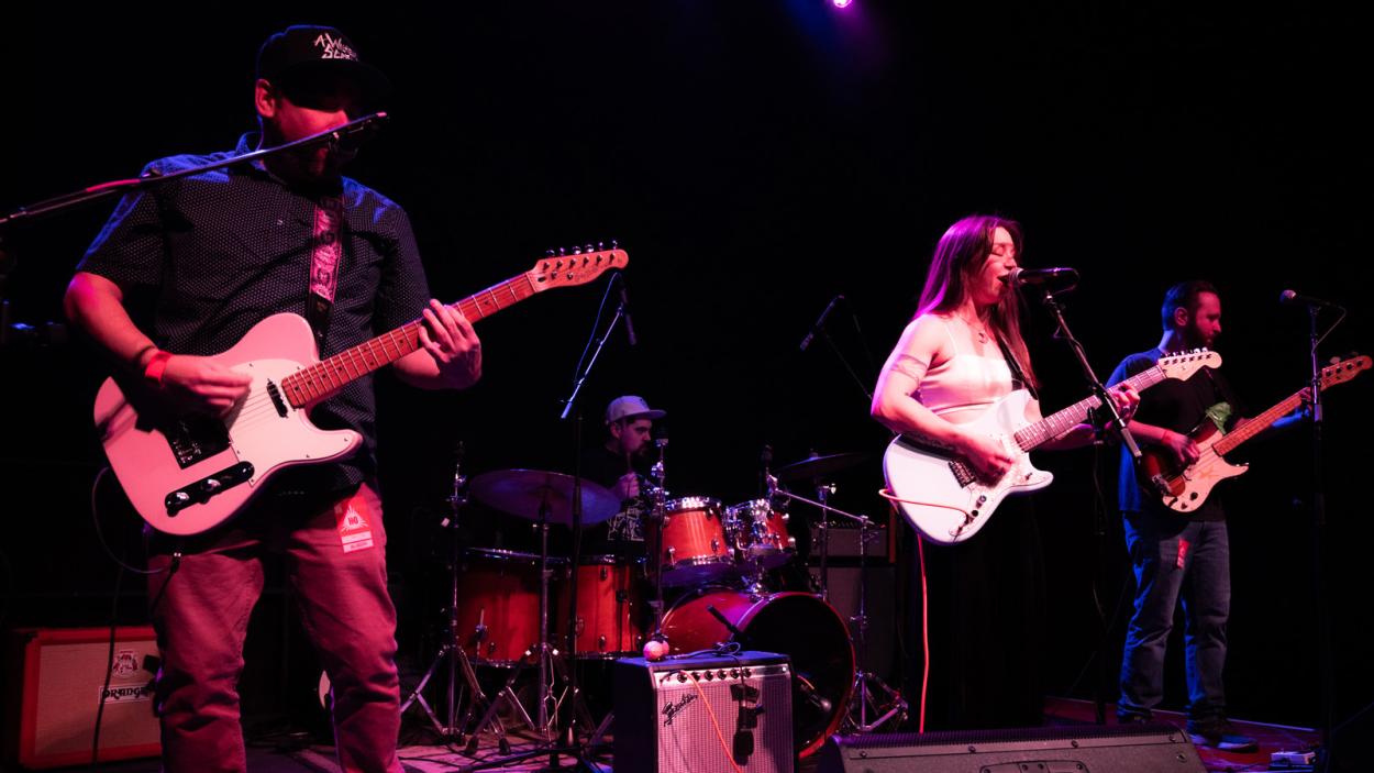 three people singing in a dark room with a pink light