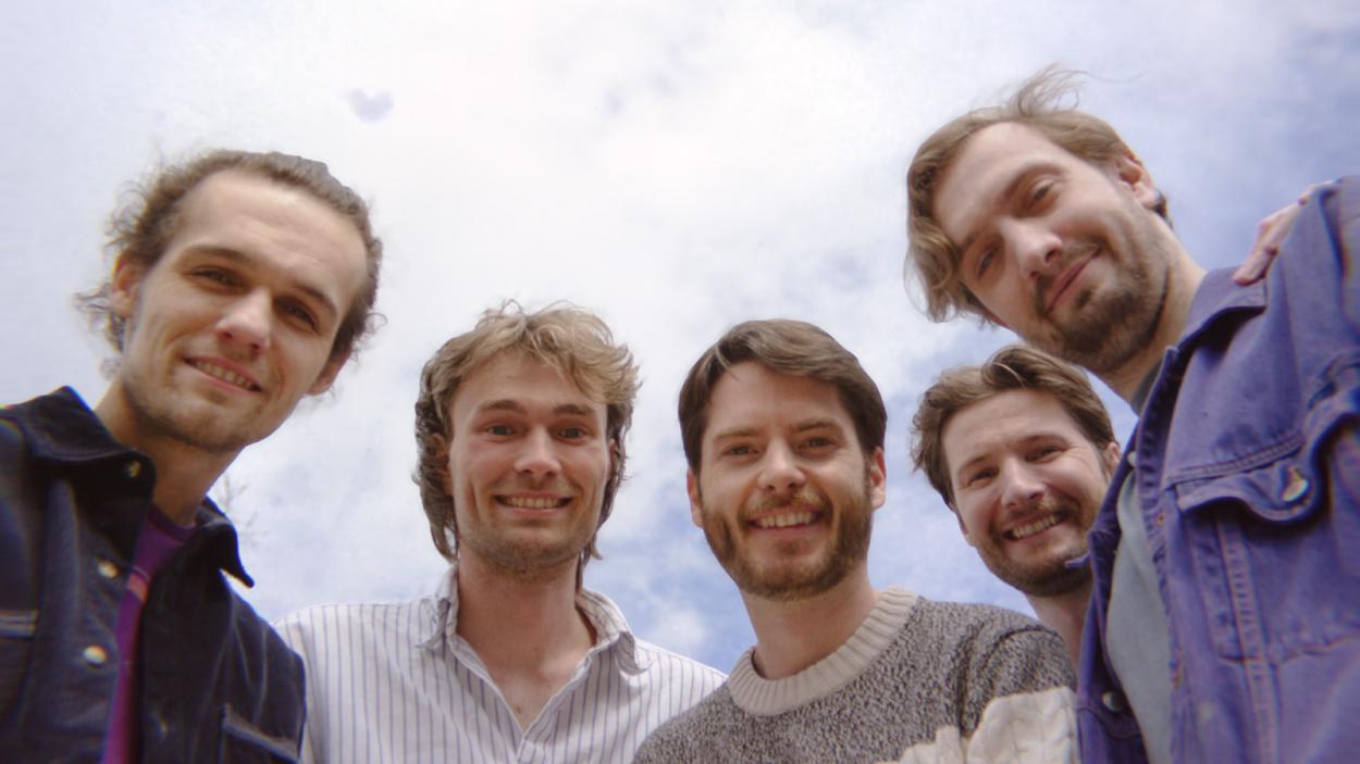five guys standing around a camera looking down with a sky background.