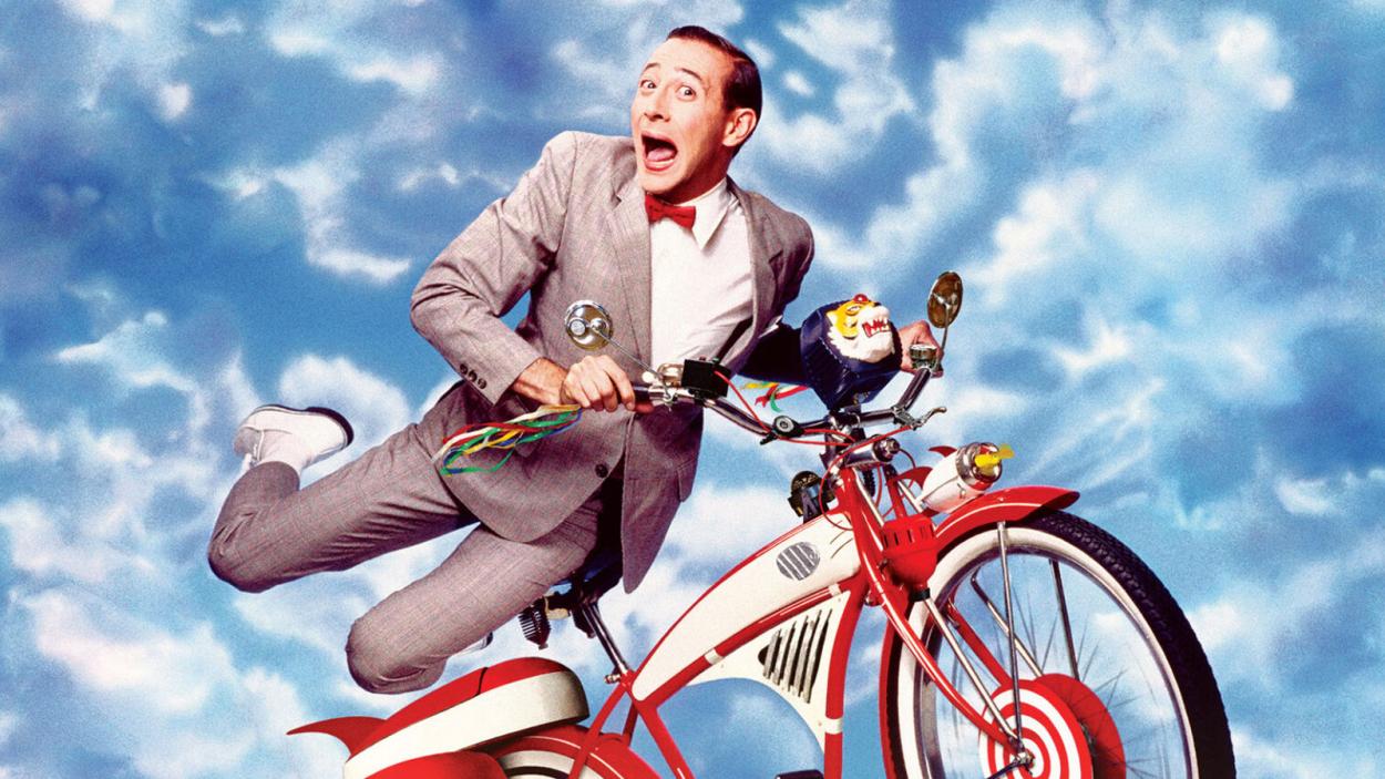 Pee-Wee Herman gleefully holding onto his precious bike as he soars through the cloudy blue sky