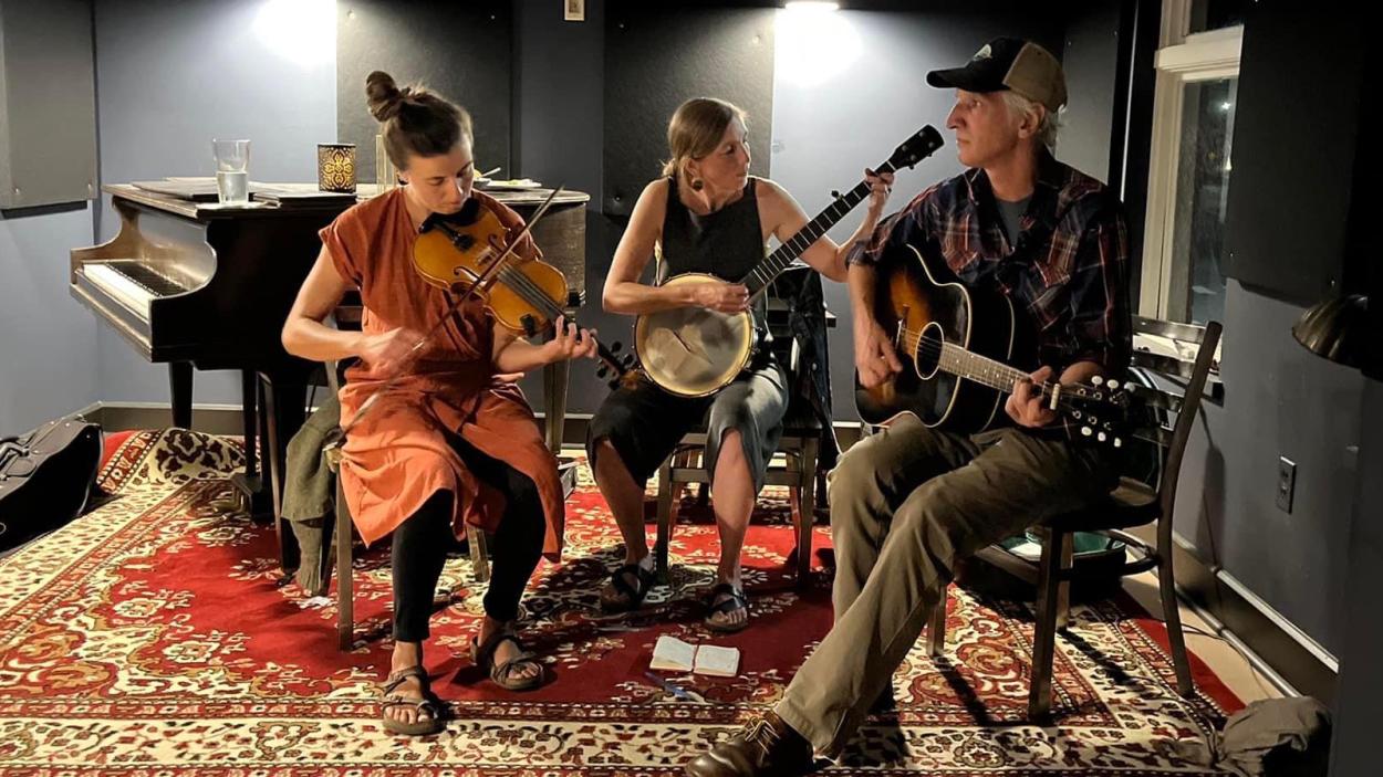 three people playing music in a grey room with a red rug