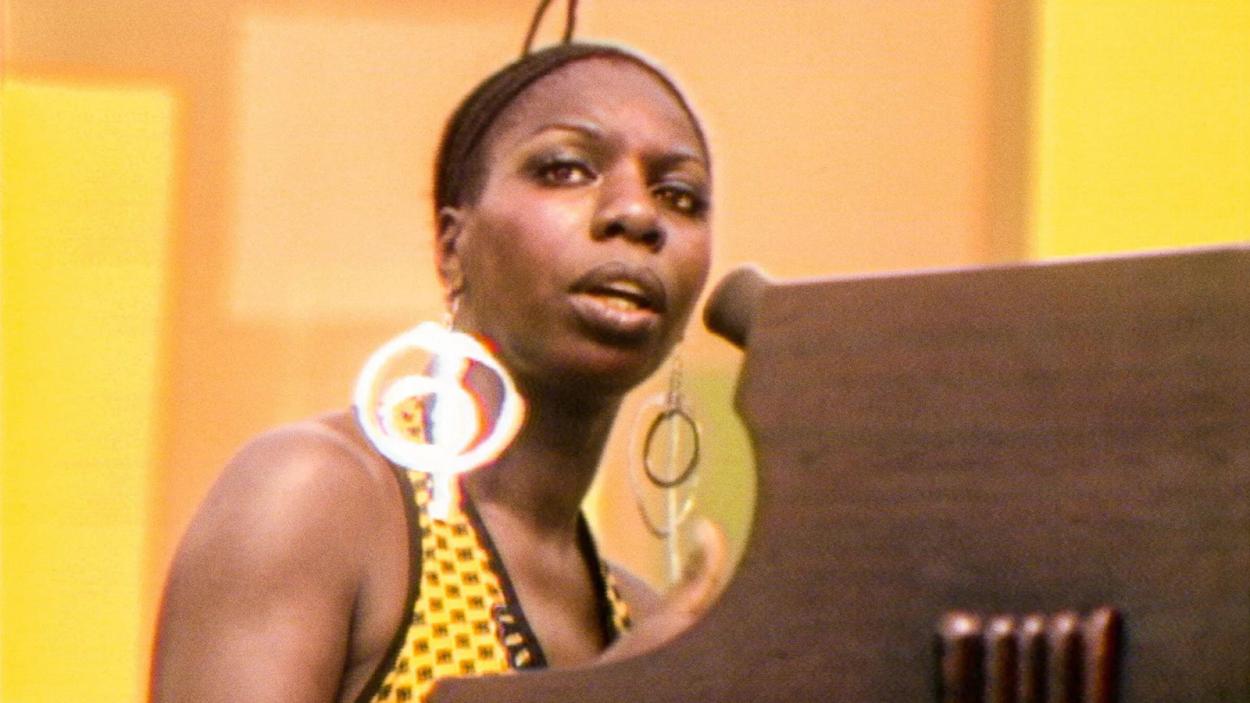 A beautiful Nina Simone sits at a piano and stares out into the crowd
