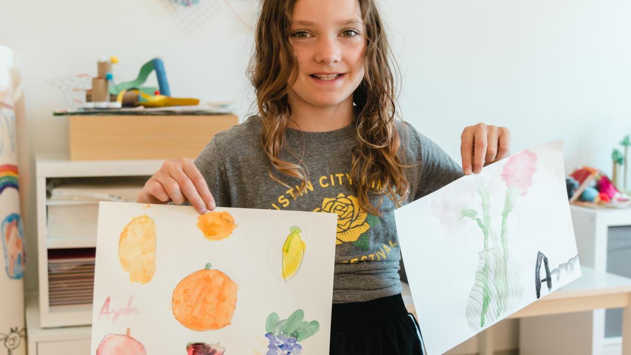 Photo of a child holding up their art work as part of Family Art Saturday
