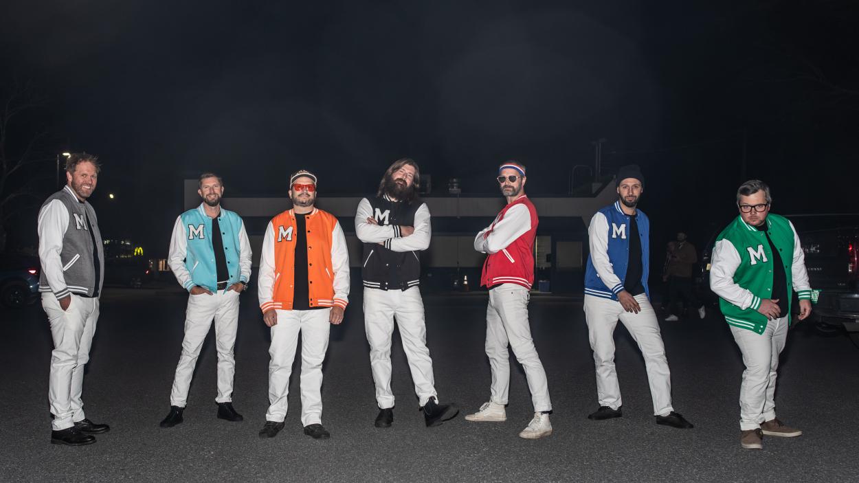 Band members pose for a photo in their colorful uniform letterman jackets.
