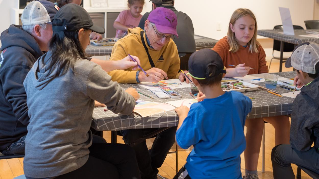 A group of adults and kids illustrate together sharing a communal table