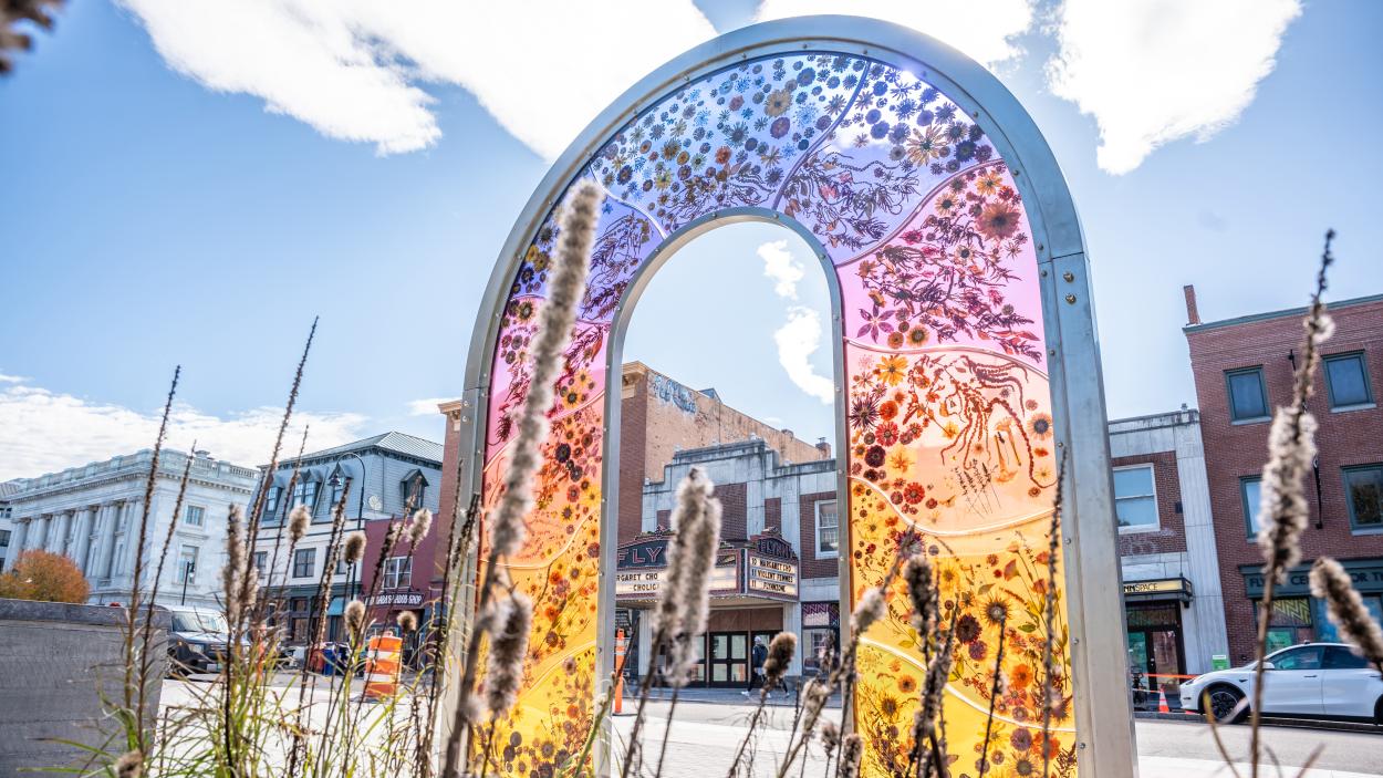 A photograph of Anthology by Lydia Kern, a sculpture on Burlington's Main Street that is a multi colored resin arch filled with flowers