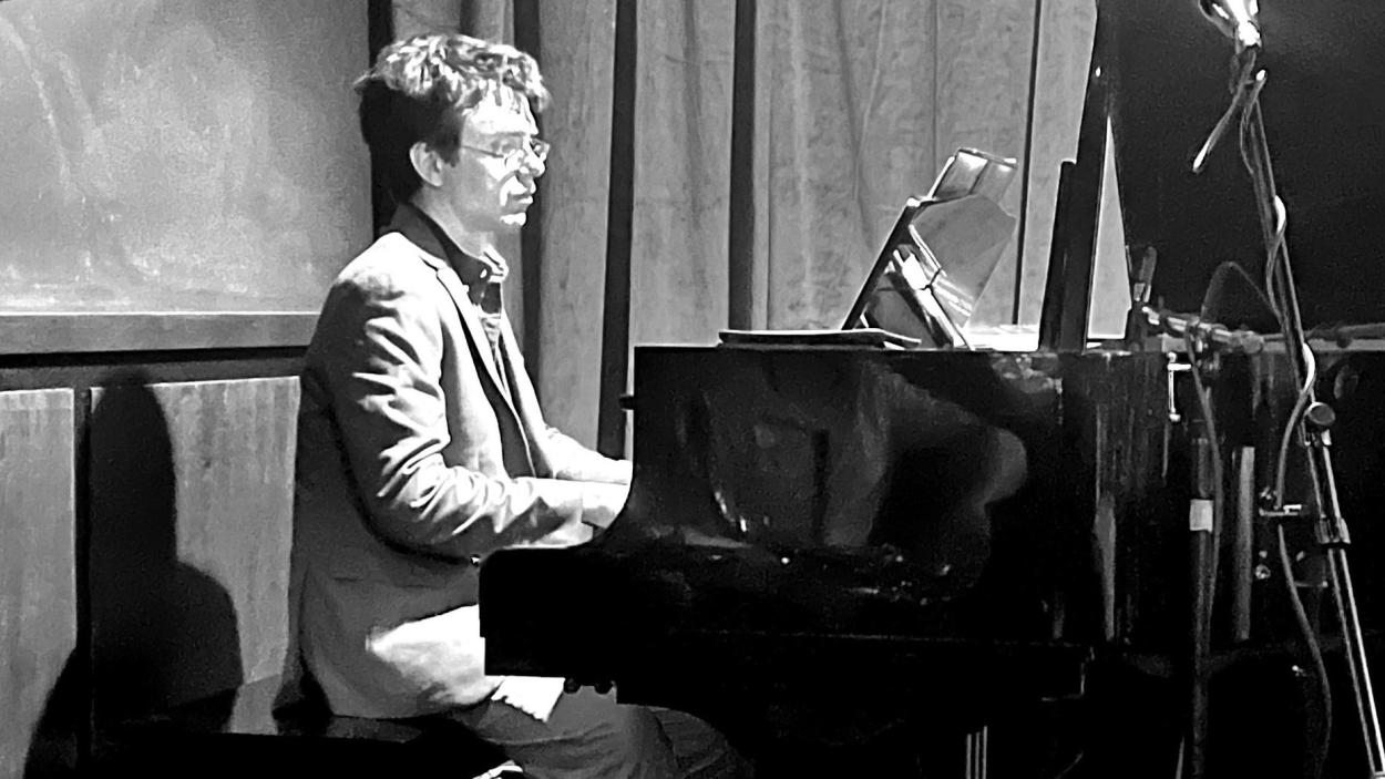 A stylized balck and while photo of a man with dark hair playing the piano