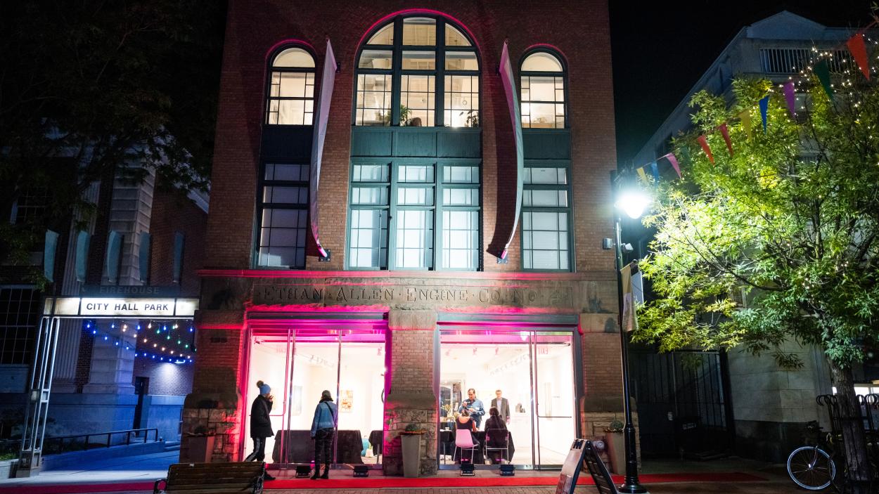A photo of the BCA Center, a brick building with three stories of tall arched windows, light up at night with blue and pink lights